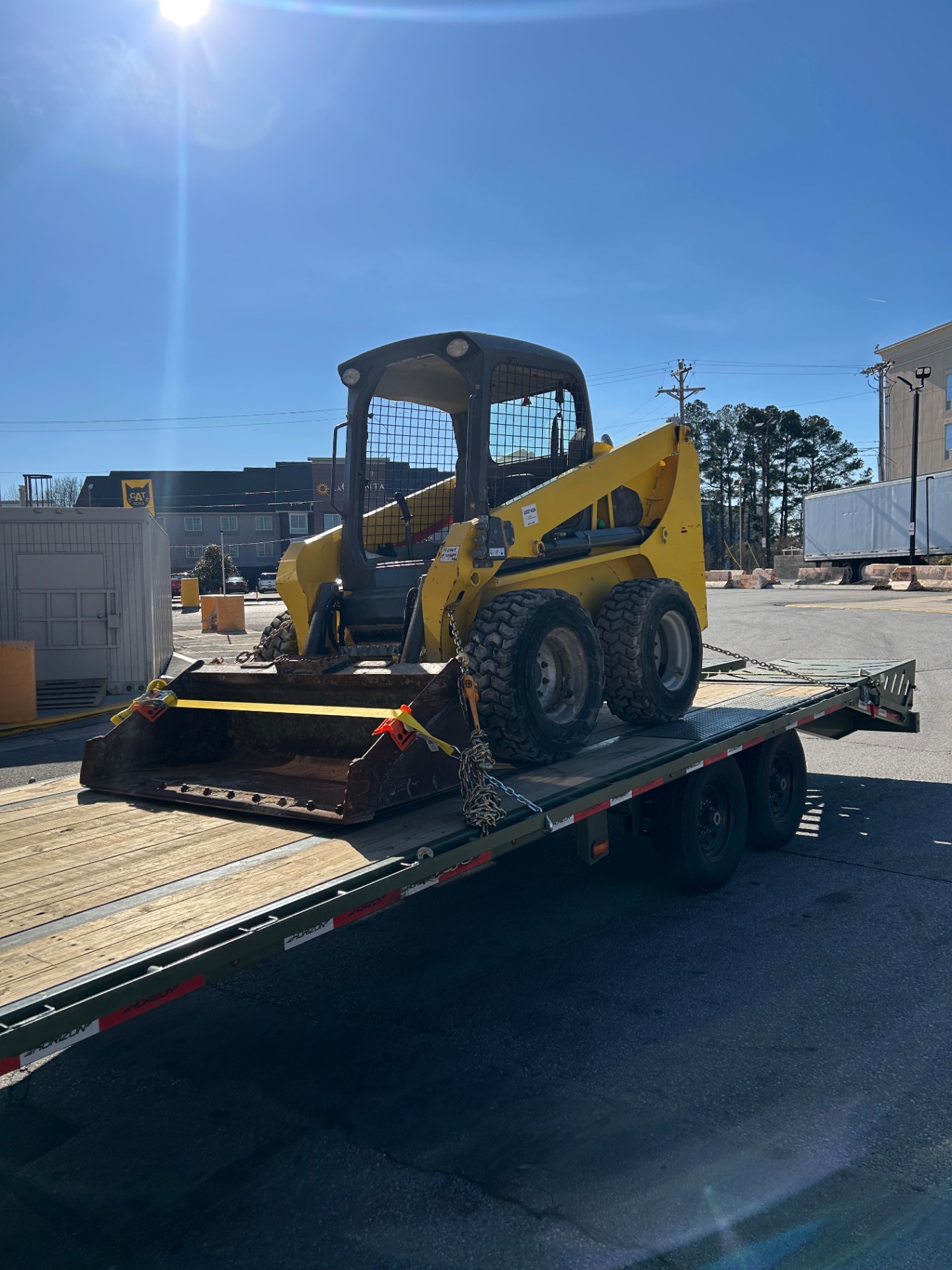 Yellow skid steer loader secured on a BigWay flatbed trailer
